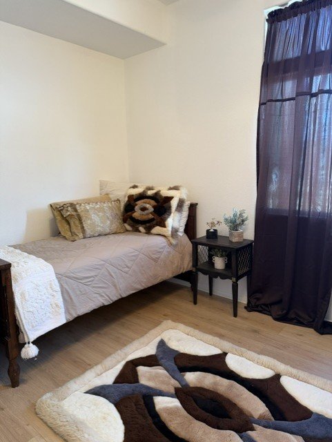 A semi-private bedroom at Wisteria RALF with layered neutral linens beneath a large window.