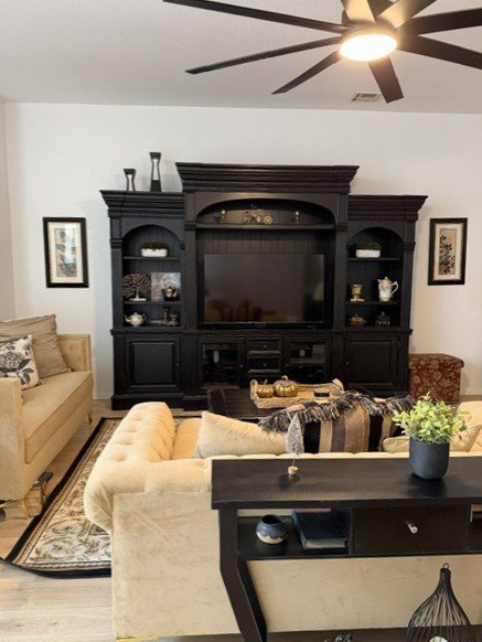 A warm living room at Wisteria RALF with a plush sofa, dark wood entertainment center, and soft ambient lighting.